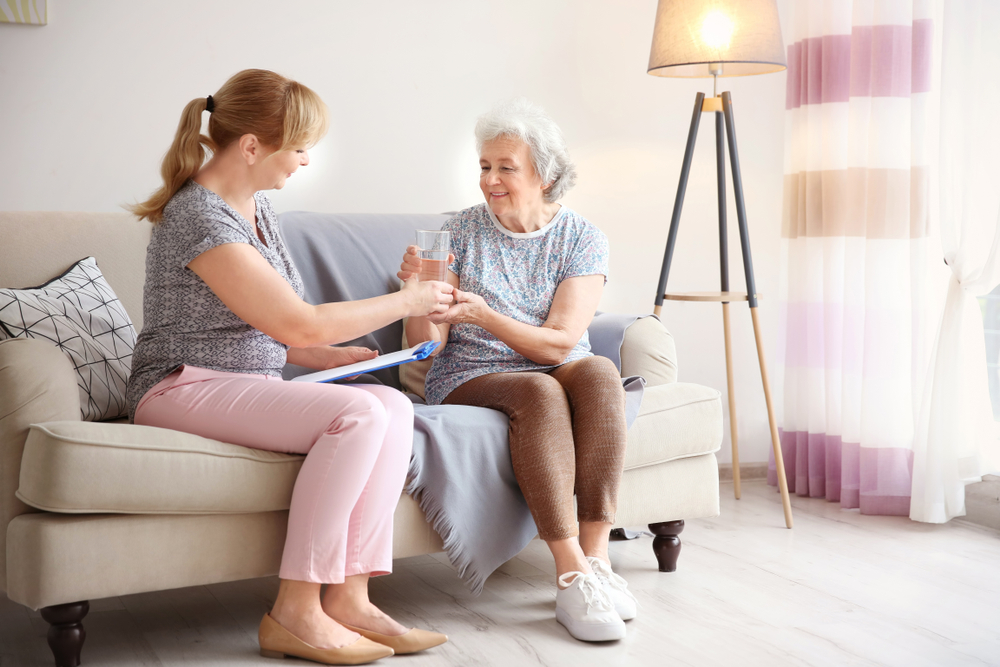caregiver gives a glass of water to the elderly woman