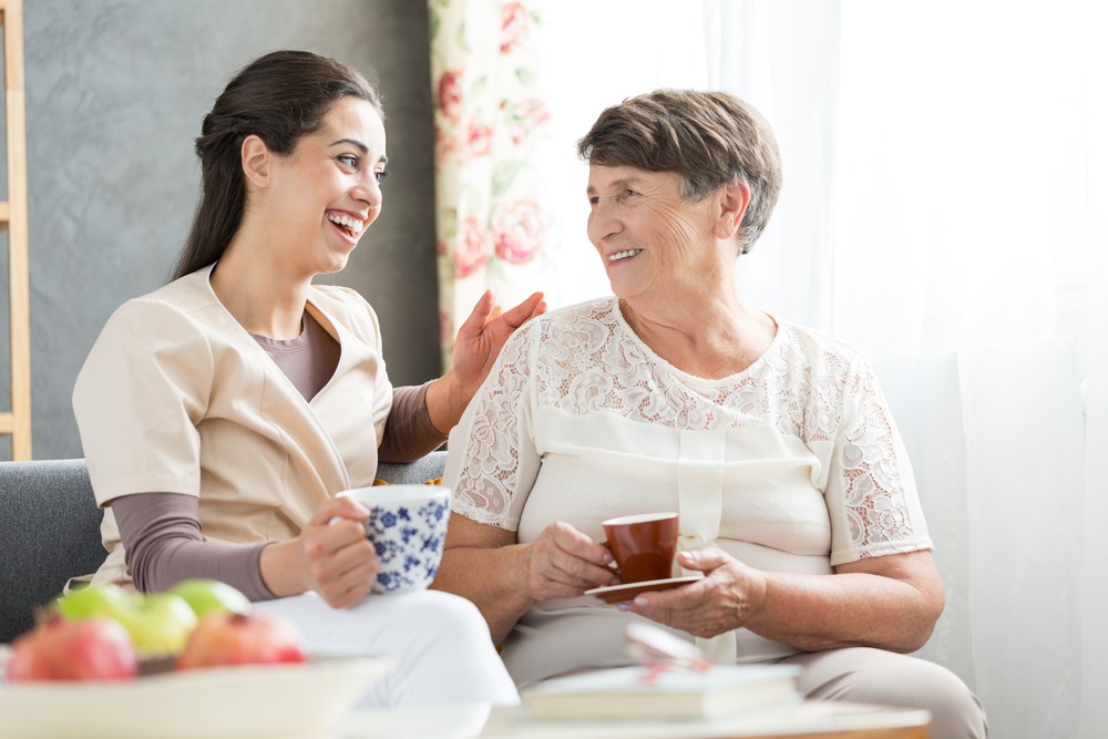 smiling caregiver drinking tea with an elderly woman